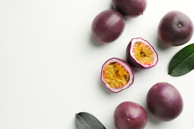 Photo of Fresh passion fruits with green leaves on white table, flat lay. Space for text