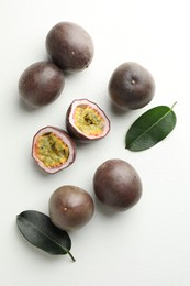 Photo of Fresh passion fruits with green leaves on white table, flat lay