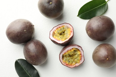 Photo of Fresh passion fruits with green leaves on white table, flat lay