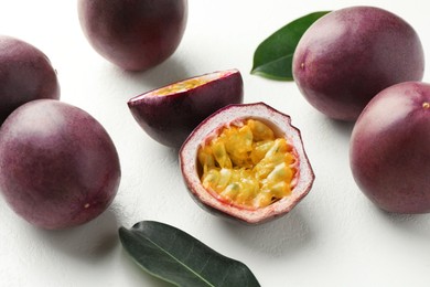 Photo of Fresh passion fruits with green leaves on white table, closeup