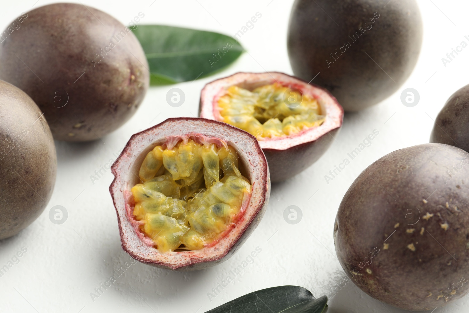 Photo of Fresh passion fruits with green leaves on white table, closeup