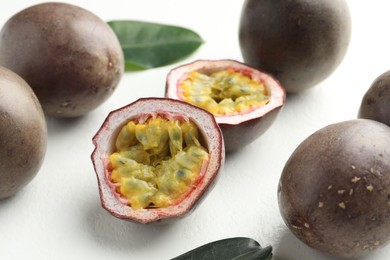 Photo of Fresh passion fruits with green leaves on white table, closeup