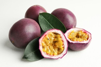 Photo of Fresh passion fruits with green leaves on white table, closeup