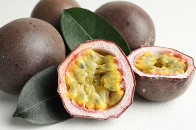 Photo of Fresh passion fruits with green leaves on white table, closeup