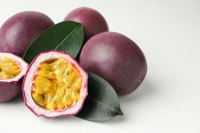 Photo of Fresh passion fruits with green leaves on white table, closeup