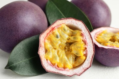 Photo of Fresh passion fruits with green leaves on white table, closeup