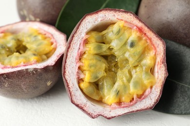 Photo of Fresh passion fruits with green leaves on white table, closeup