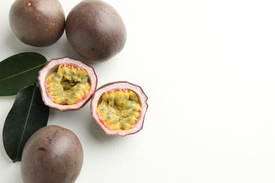 Photo of Fresh passion fruits with green leaves on white table, flat lay. Space for text