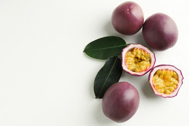 Photo of Fresh passion fruits with green leaves on white table, flat lay. Space for text