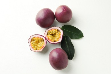 Photo of Fresh passion fruits with green leaves on white table, flat lay
