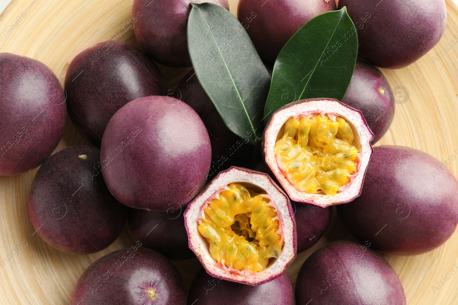 Fresh passion fruits with green leaves on plate, closeup Photo of Fresh passion fruits with green leaves on plate, closeup