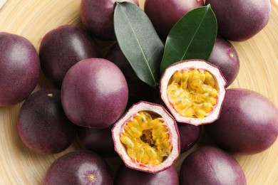 Photo of Fresh passion fruits with green leaves on plate, closeup