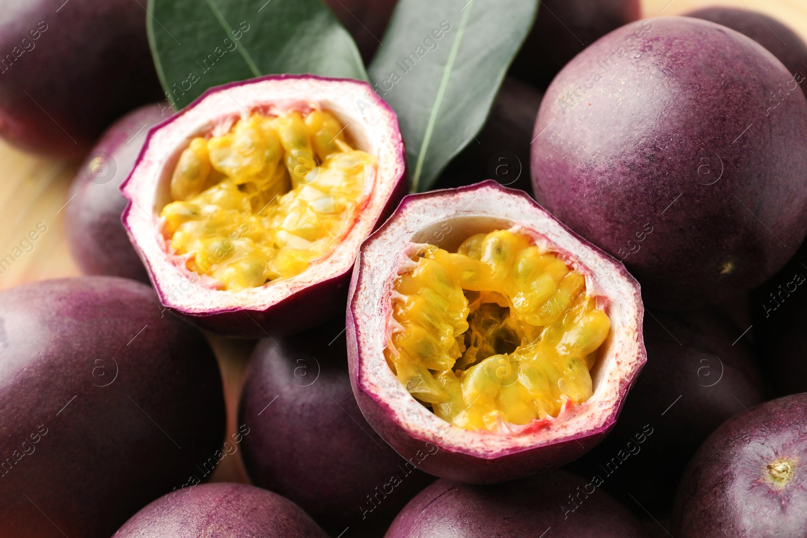 Photo of Fresh passion fruits with green leaves on table, closeup