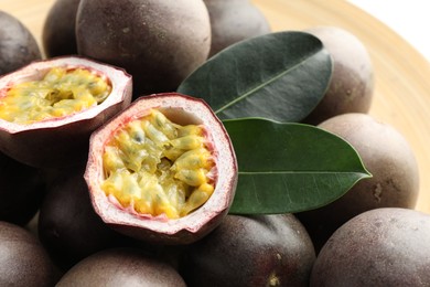 Photo of Fresh passion fruits with green leaves on plate, closeup