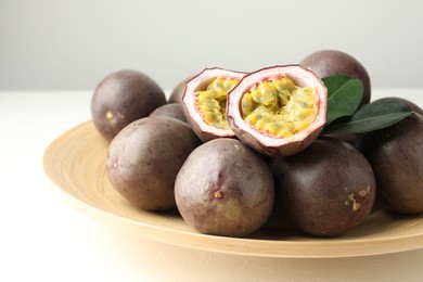 Photo of Fresh passion fruits with green leaves on white table, closeup