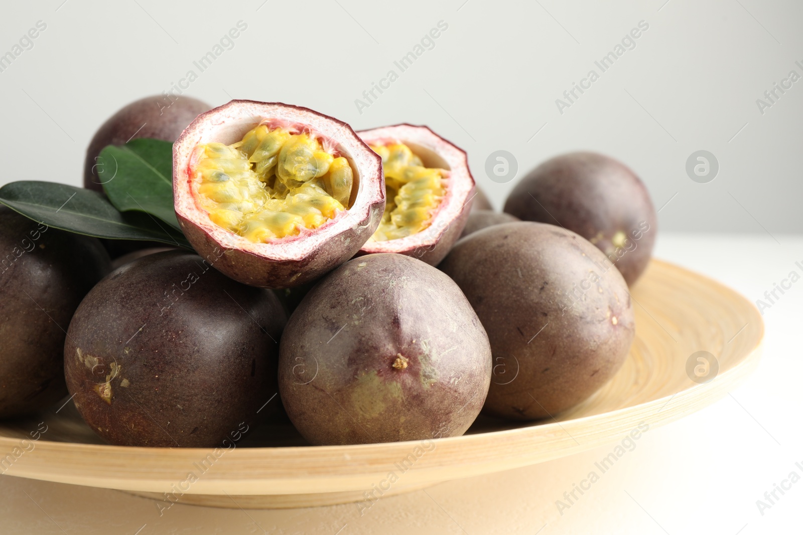 Photo of Fresh passion fruits with green leaves on white table, closeup
