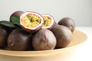Photo of Fresh passion fruits with green leaves on white table, closeup