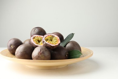 Photo of Fresh passion fruits with green leaves on white table
