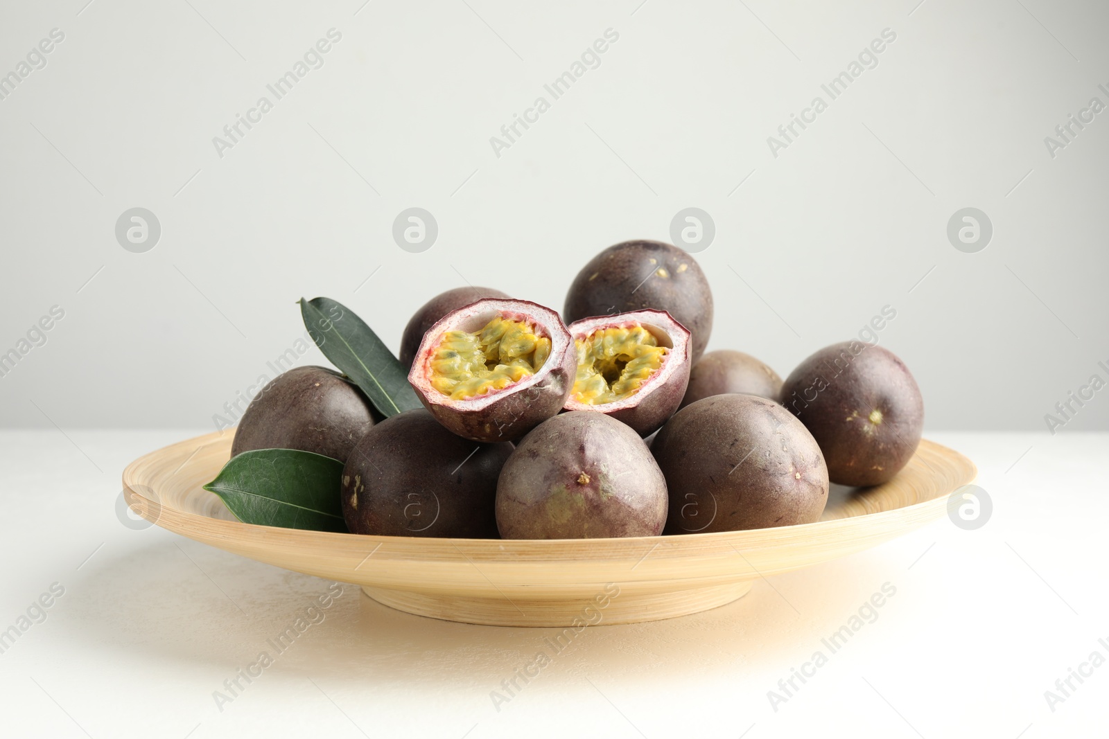 Fresh passion fruits with green leaves on white table Photo of Fresh passion fruits with green leaves on white table