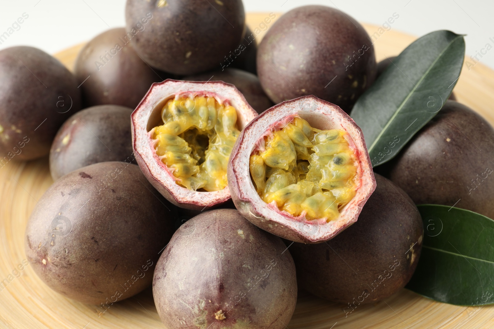 Fresh passion fruits with green leaves on plate, closeup Photo of Fresh passion fruits with green leaves on plate, closeup