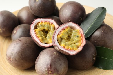 Photo of Fresh passion fruits with green leaves on plate, closeup