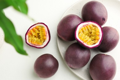 Photo of Fresh passion fruits with green leaves on white table, flat lay