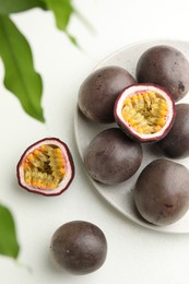 Photo of Fresh passion fruits with green leaves on white table, flat lay