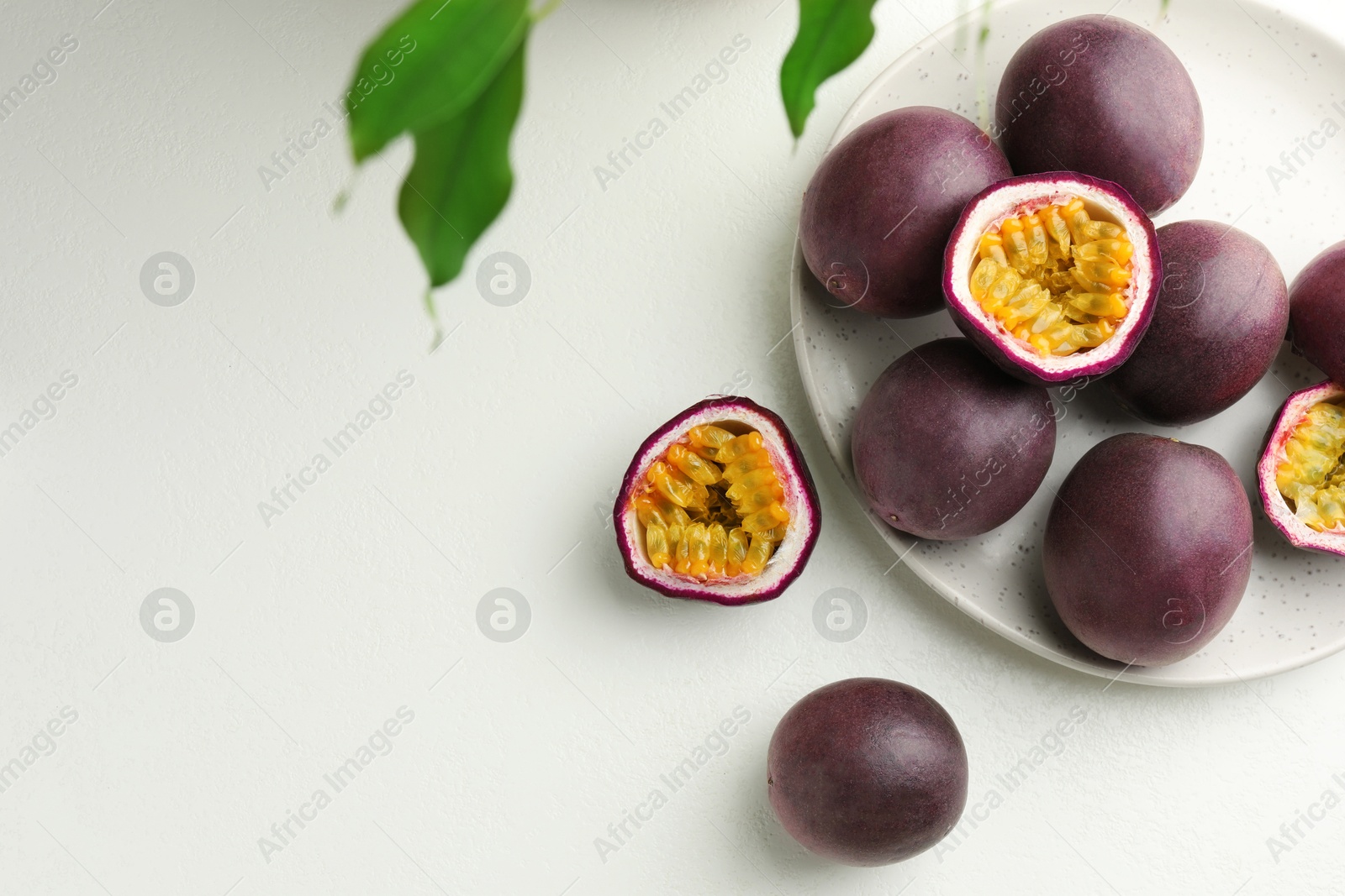 Photo of Fresh passion fruits with green leaves on white table, flat lay. Space for text