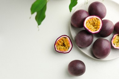 Photo of Fresh passion fruits with green leaves on white table, flat lay. Space for text