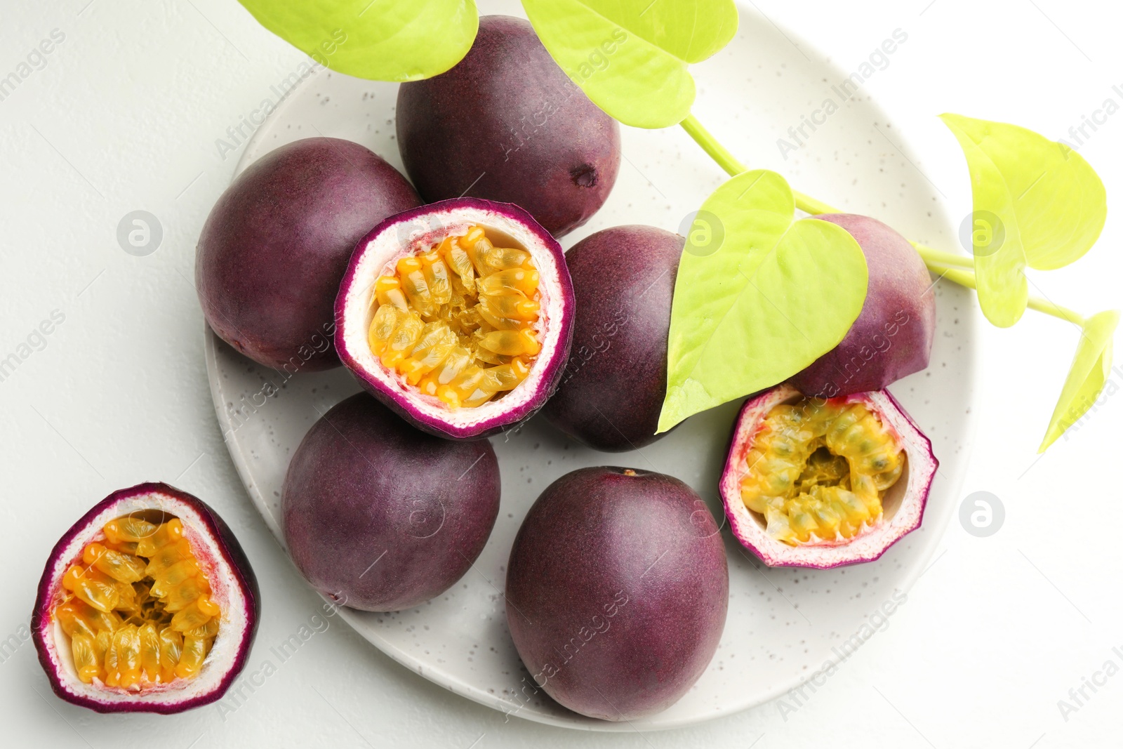 Fresh passion fruits with green leaves on white table, flat lay Photo of Fresh passion fruits with green leaves on white table, flat lay