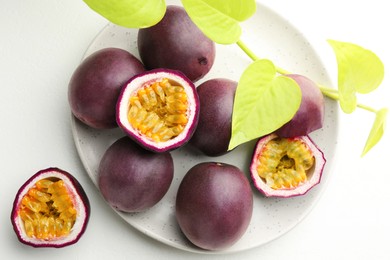 Photo of Fresh passion fruits with green leaves on white table, flat lay