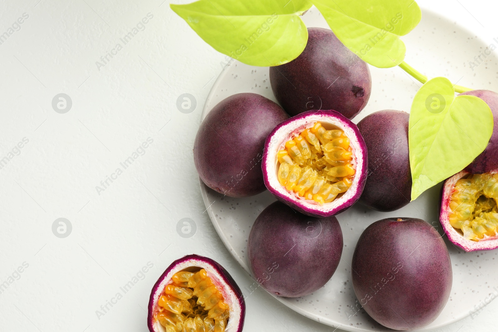 Fresh passion fruits with green leaves on white table, above view. Space for text Photo of Fresh passion fruits with green leaves on white table, above view. Space for text