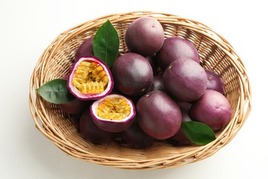 Photo of Fresh passion fruits with green leaves in wicker basket on white table, above view