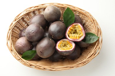 Photo of Fresh passion fruits with green leaves in wicker basket on white table, above view