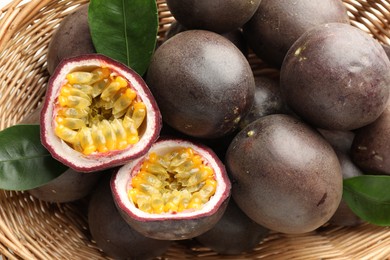 Photo of Fresh passion fruits with green leaves in wicker basket, closeup