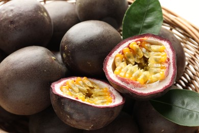 Photo of Fresh passion fruits with green leaves in wicker basket, closeup