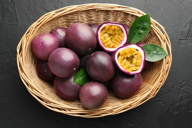 Photo of Fresh passion fruits with green leaves in wicker basket on grey textured table, top view