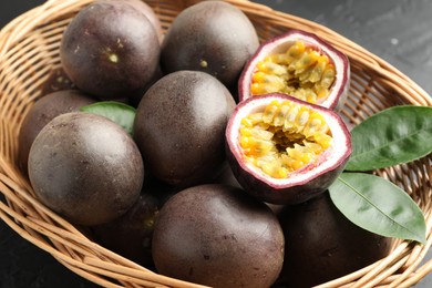 Photo of Fresh passion fruits with green leaves in wicker basket on grey table, closeup