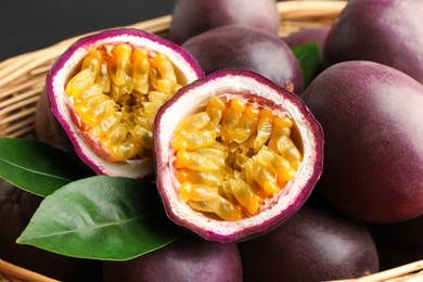 Photo of Fresh passion fruits with green leaves in wicker basket, closeup