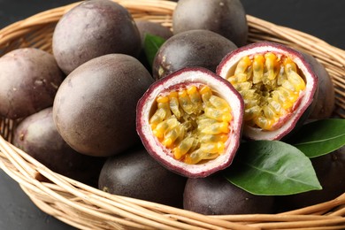 Photo of Fresh passion fruits with green leaves in wicker basket on grey table, closeup