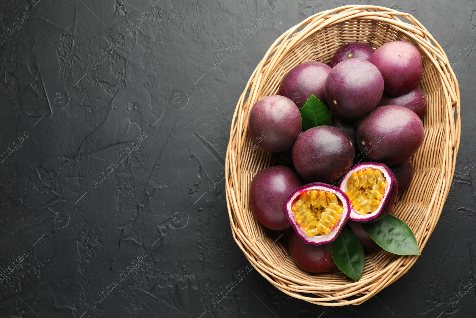 Fresh passion fruits with green leaves in wicker basket on grey textured table, top view. Space for text Photo of Fresh passion fruits with green leaves in wicker basket on grey textured table, top view. Space for text