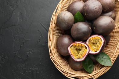 Photo of Fresh passion fruits with green leaves in wicker basket on grey textured table, top view. Space for text
