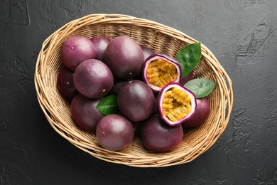 Photo of Fresh passion fruits with green leaves in wicker basket on grey textured table, top view