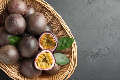 Photo of Fresh passion fruits with green leaves in wicker basket on grey textured table, top view. Space for text