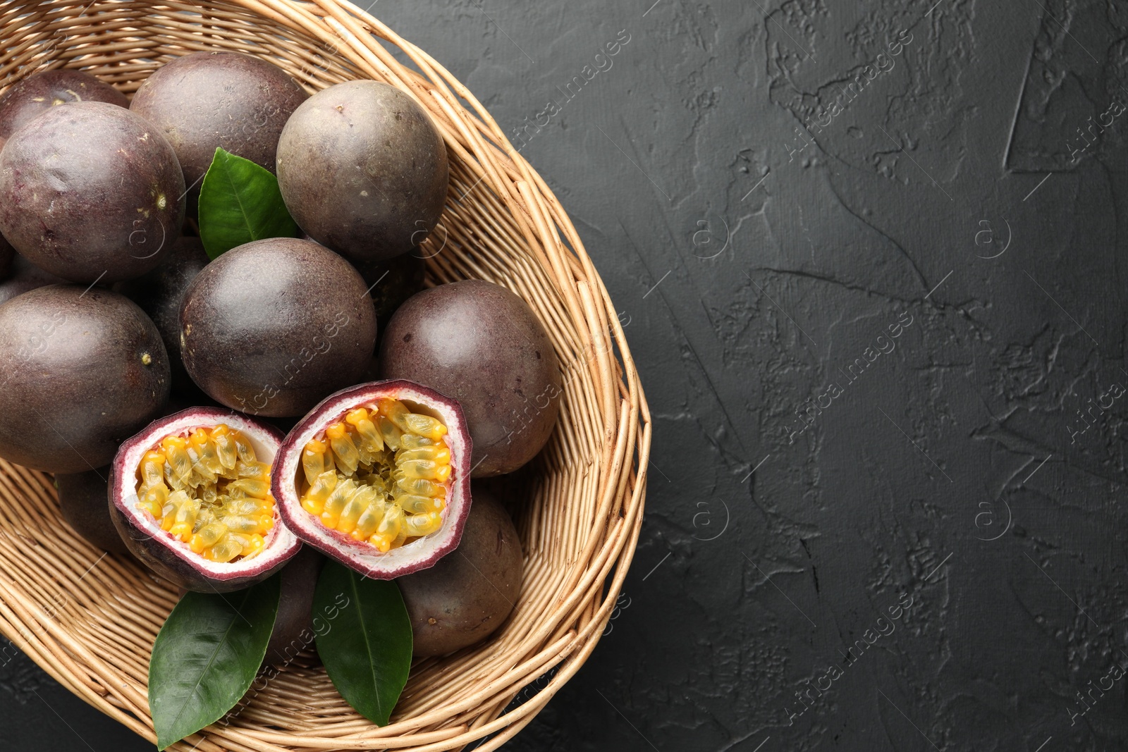 Fresh passion fruits with green leaves in wicker basket on grey textured table, top view. Space for text Photo of Fresh passion fruits with green leaves in wicker basket on grey textured table, top view. Space for text