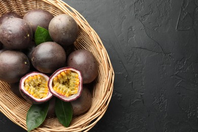 Photo of Fresh passion fruits with green leaves in wicker basket on grey textured table, top view. Space for text