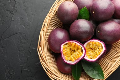 Photo of Fresh passion fruits with green leaves in wicker basket on grey textured table, top view. Space for text