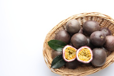 Photo of Fresh passion fruits with green leaves in wicker basket on white background, top view. Space for text