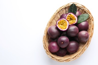 Photo of Fresh passion fruits with green leaves in wicker basket on white background, top view. Space for text