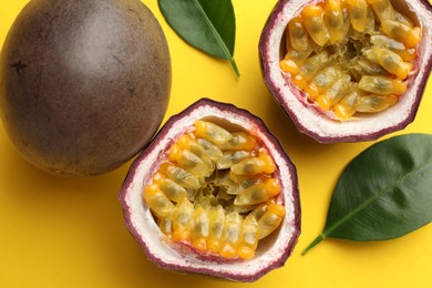 Photo of Fresh passion fruits with green leaves on yellow background, closeup